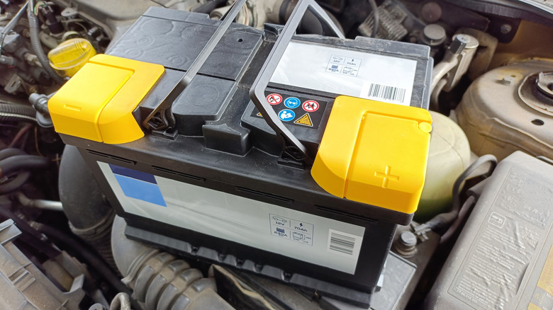 A disconnected 12V car battery placed on top of the engine compartment